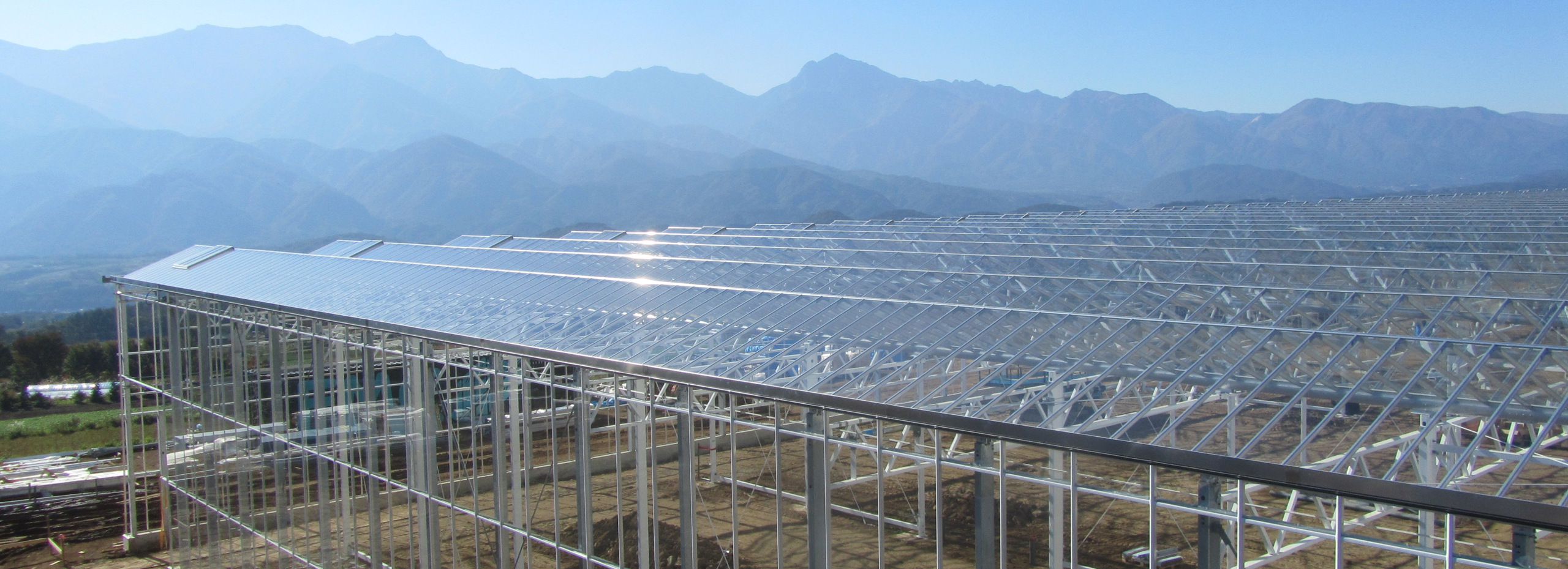 a glass greenhouse under construction in Japan with mountains in the background