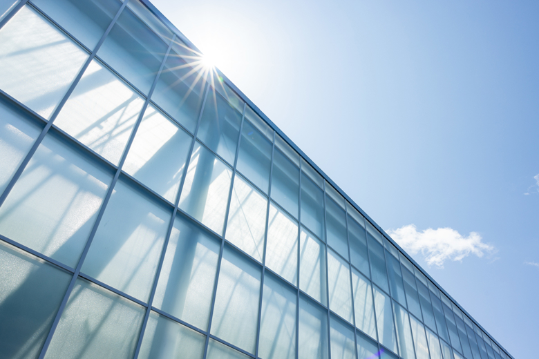 facade view of glass greenhouse with shining sun and blue sky