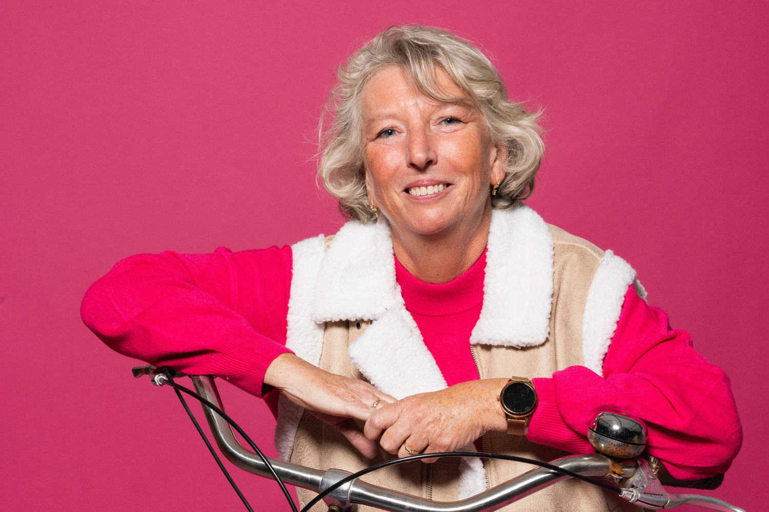 lachende dame voor roze achtergrond poseert met haar blauwe fiets